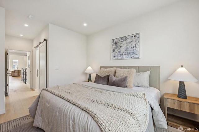 bedroom with a barn door, wood finished floors, and recessed lighting