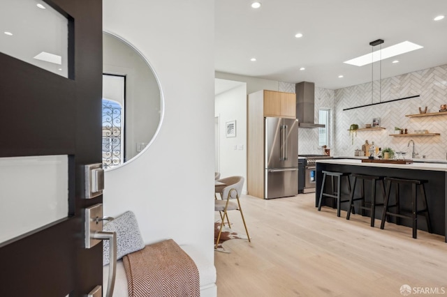 kitchen with wall chimney exhaust hood, high end appliances, a skylight, tasteful backsplash, and recessed lighting