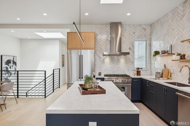 kitchen featuring premium appliances, a sink, wall chimney range hood, a skylight, and tasteful backsplash