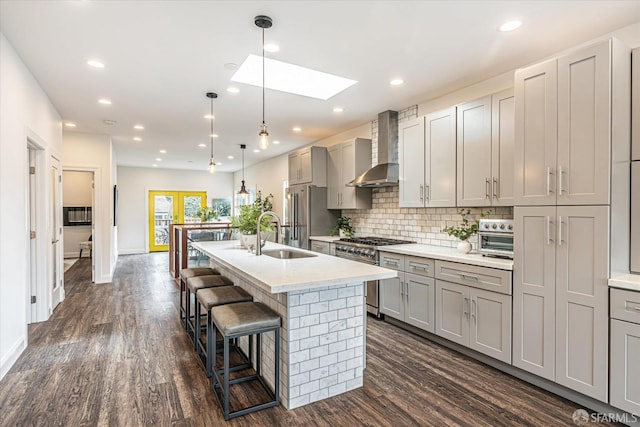 kitchen featuring high quality appliances, gray cabinetry, a center island with sink, and wall chimney exhaust hood