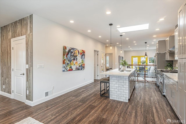 kitchen with high end range, a skylight, gray cabinets, an island with sink, and pendant lighting