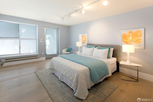 bedroom featuring track lighting, baseboard heating, light wood-style flooring, and baseboards