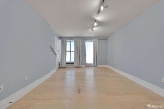 empty room featuring track lighting, light wood-style flooring, and baseboards