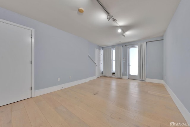 spare room featuring rail lighting, hardwood / wood-style flooring, and baseboards