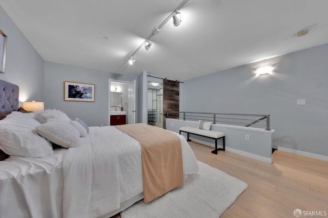 bedroom with wood finished floors, rail lighting, baseboards, and ensuite bathroom