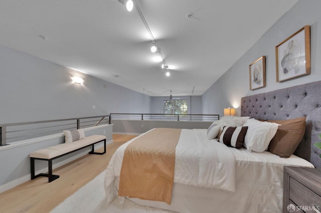 bedroom with wood finished floors, track lighting, and baseboards
