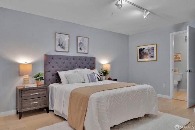 bedroom with light wood finished floors, rail lighting, baseboards, and ensuite bathroom