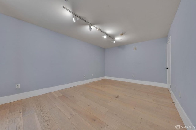 unfurnished room featuring light wood-type flooring, track lighting, and baseboards