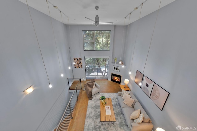 living room with ceiling fan, a fireplace, rail lighting, and a towering ceiling
