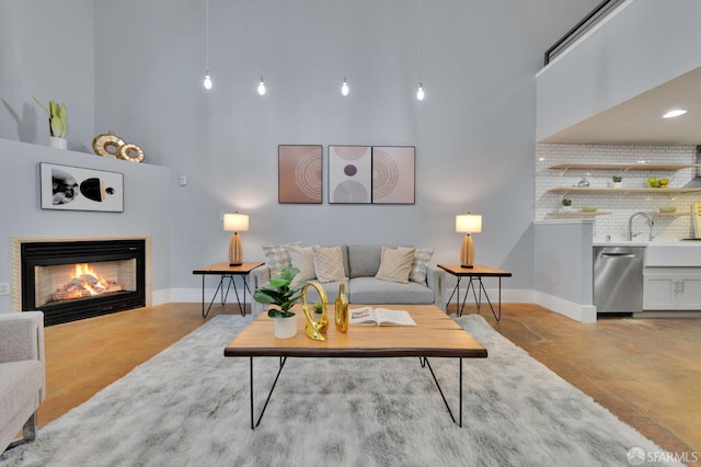living area with a high ceiling, finished concrete floors, baseboards, and a glass covered fireplace