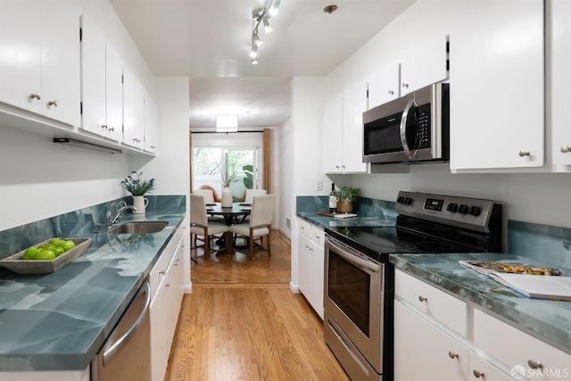 kitchen featuring stainless steel counters, light wood-style flooring, white cabinets, appliances with stainless steel finishes, and a sink