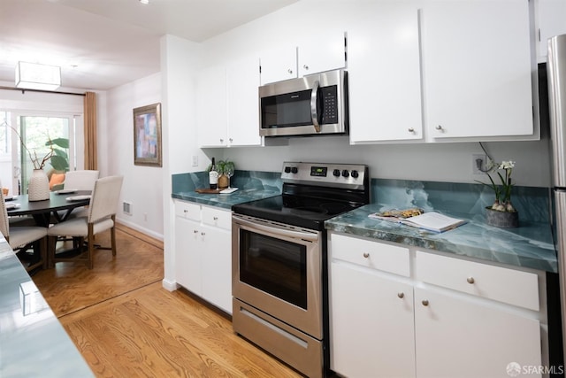 kitchen featuring visible vents, white cabinets, baseboards, parquet flooring, and stainless steel appliances