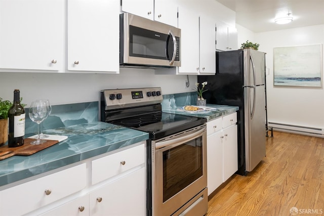 kitchen with light wood-type flooring, appliances with stainless steel finishes, stainless steel countertops, white cabinetry, and a baseboard heating unit