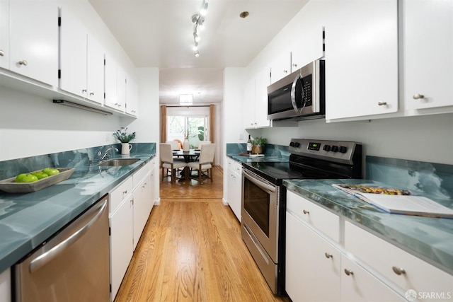 kitchen with light wood-style floors, track lighting, white cabinetry, appliances with stainless steel finishes, and a sink