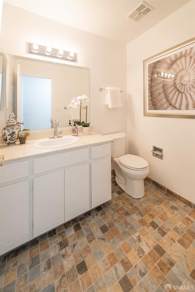 bathroom with visible vents, toilet, vanity, and stone finish flooring