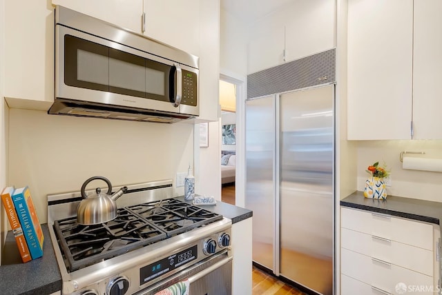 2201 Sacramento St Unit 404, San Francisco, CA 94115 - kitchen featuring light wood-style flooring, white cabinetry, appliances with stainless steel finishes, and dark countertops