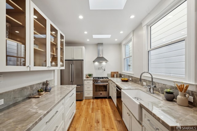 1980-1982 Fell St, San Francisco, CA 94117 - kitchen with stainless steel appliances, a skylight, wall chimney range hood, light wood finished floors, and white cabinets