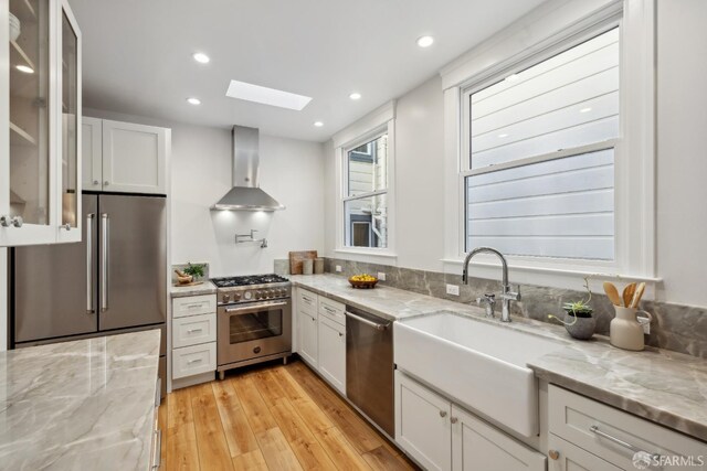1980-1982 Fell St, San Francisco, CA 94117 - kitchen featuring wall chimney range hood, appliances with stainless steel finishes, a skylight, a sink, and light wood-style flooring