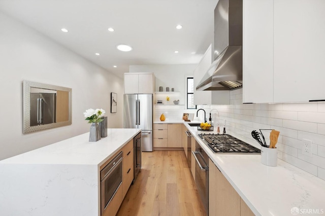 kitchen featuring white cabinetry, sink, wall chimney exhaust hood, stainless steel appliances, and light hardwood / wood-style flooring