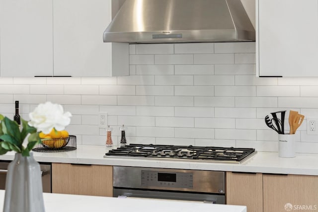 kitchen with backsplash, wall chimney range hood, wall oven, light stone counters, and stainless steel gas cooktop