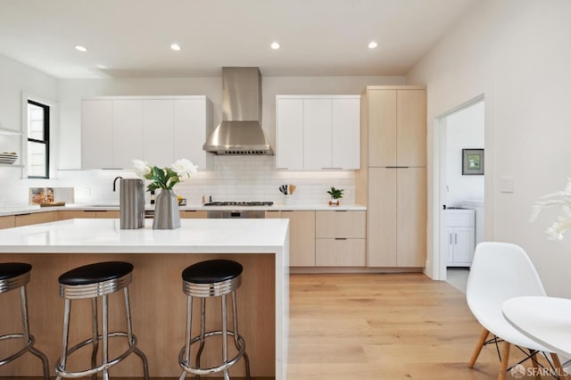 kitchen featuring a center island, wall chimney exhaust hood, light hardwood / wood-style floors, and white cabinetry