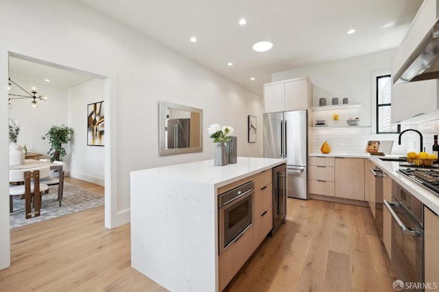 kitchen with sink, a center island, light hardwood / wood-style flooring, extractor fan, and appliances with stainless steel finishes