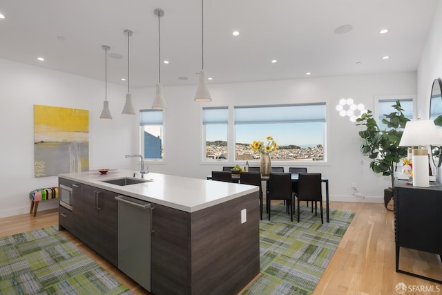 kitchen with sink, a kitchen island with sink, dark brown cabinets, light hardwood / wood-style floors, and stainless steel dishwasher