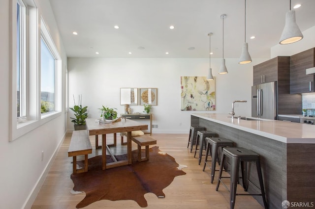 kitchen featuring dark brown cabinetry, sink, light wood-type flooring, stainless steel refrigerator, and pendant lighting