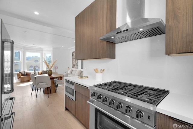 kitchen featuring appliances with stainless steel finishes, light hardwood / wood-style flooring, ornamental molding, and wall chimney range hood