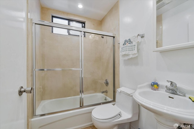 bathroom featuring a sink, bath / shower combo with glass door, and toilet