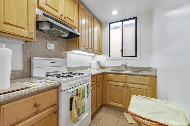 kitchen featuring gas range gas stove, light countertops, under cabinet range hood, a sink, and light tile patterned floors