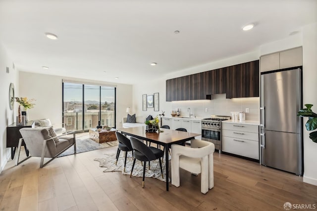 kitchen featuring sink, backsplash, stainless steel appliances, light hardwood / wood-style floors, and dark brown cabinetry