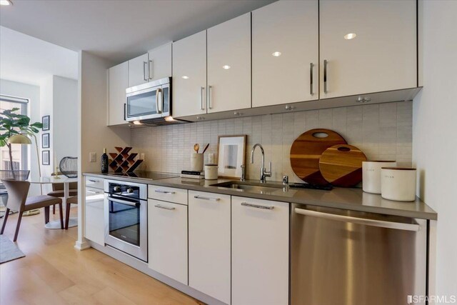 kitchen featuring a sink, stainless steel appliances, white cabinets, light wood-style floors, and backsplash