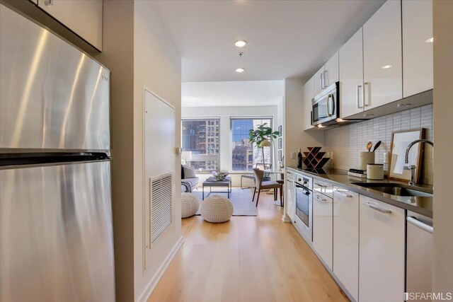 kitchen featuring tasteful backsplash, light wood-style flooring, appliances with stainless steel finishes, white cabinetry, and a sink