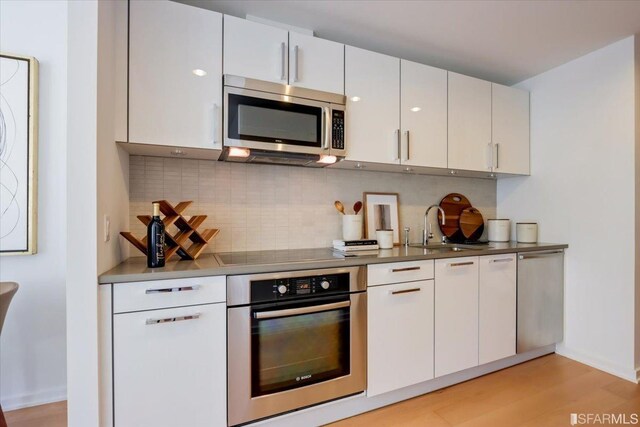 kitchen with tasteful backsplash, appliances with stainless steel finishes, light wood-style floors, white cabinetry, and a sink