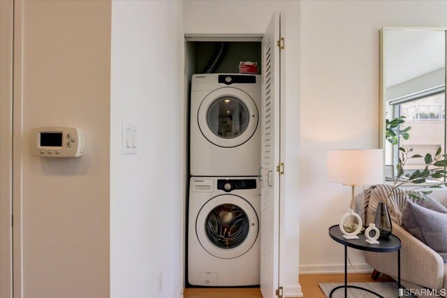 clothes washing area featuring laundry area, wood finished floors, baseboards, and stacked washer and dryer