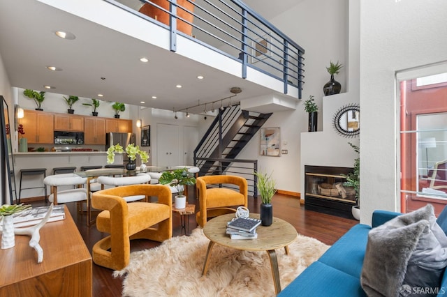 living room with dark hardwood / wood-style flooring, a towering ceiling, plenty of natural light, and rail lighting