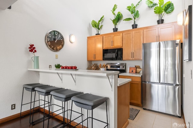 kitchen featuring a kitchen breakfast bar, kitchen peninsula, light tile patterned floors, and stainless steel appliances