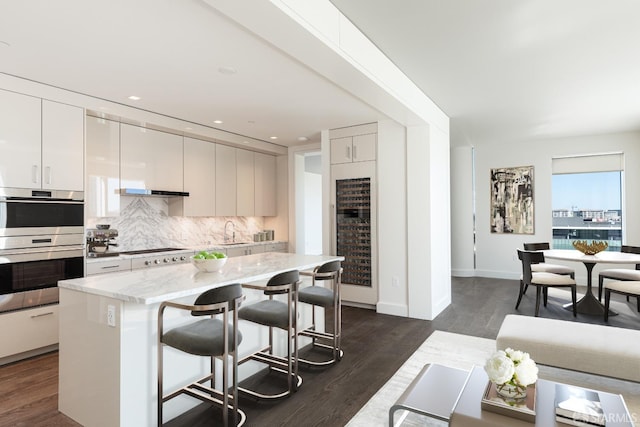 kitchen featuring decorative backsplash, a sink, dark wood-style flooring, and stainless steel double oven