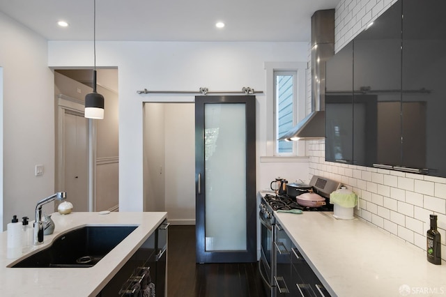 kitchen featuring double oven range, wall chimney range hood, sink, a barn door, and decorative light fixtures