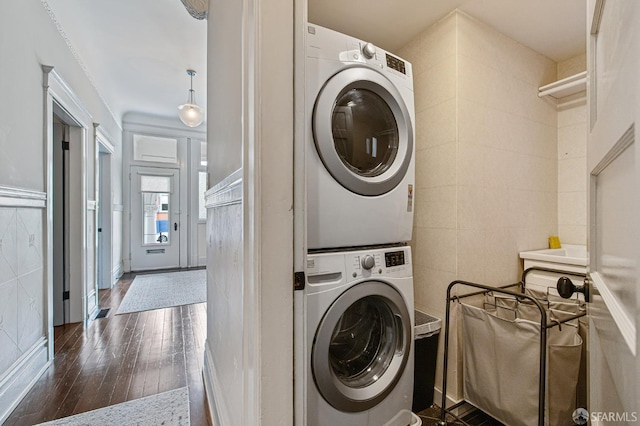 clothes washing area featuring dark hardwood / wood-style floors, stacked washer and dryer, and tile walls