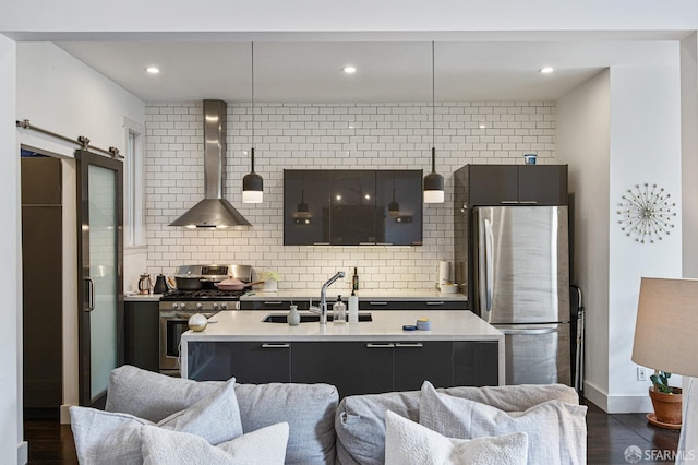 kitchen with sink, wall chimney exhaust hood, stainless steel appliances, tasteful backsplash, and a barn door