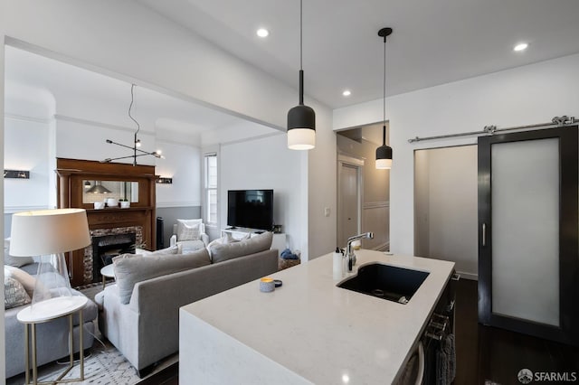 kitchen featuring pendant lighting, a center island with sink, sink, light stone countertops, and a chandelier