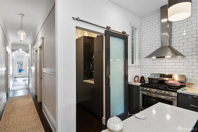 kitchen with wall chimney exhaust hood, a barn door, stainless steel range with gas cooktop, pendant lighting, and decorative backsplash