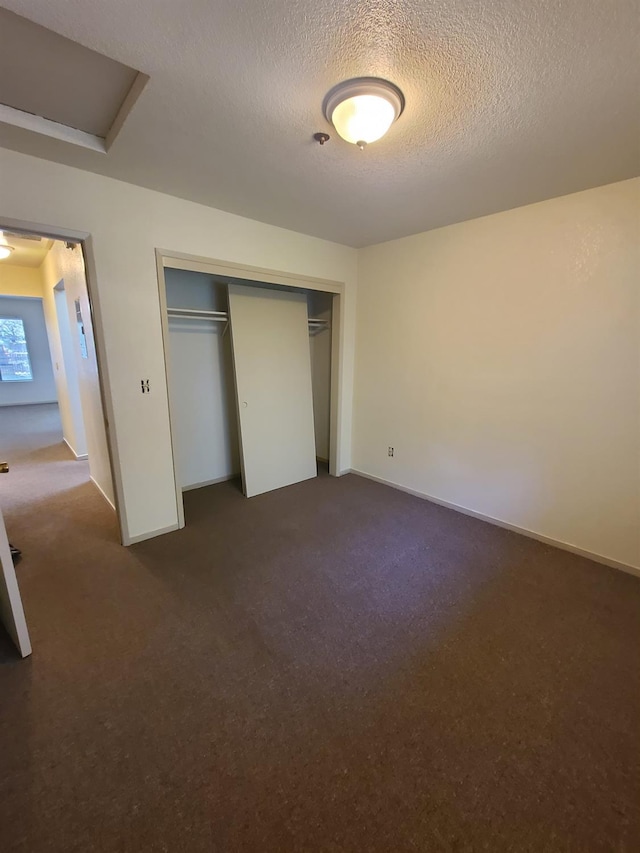 unfurnished bedroom featuring a closet, dark carpet, attic access, a textured ceiling, and baseboards