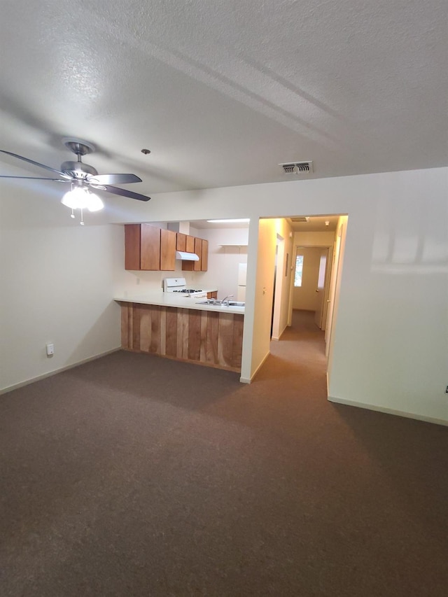 kitchen featuring visible vents, brown cabinets, a peninsula, a textured ceiling, and white range