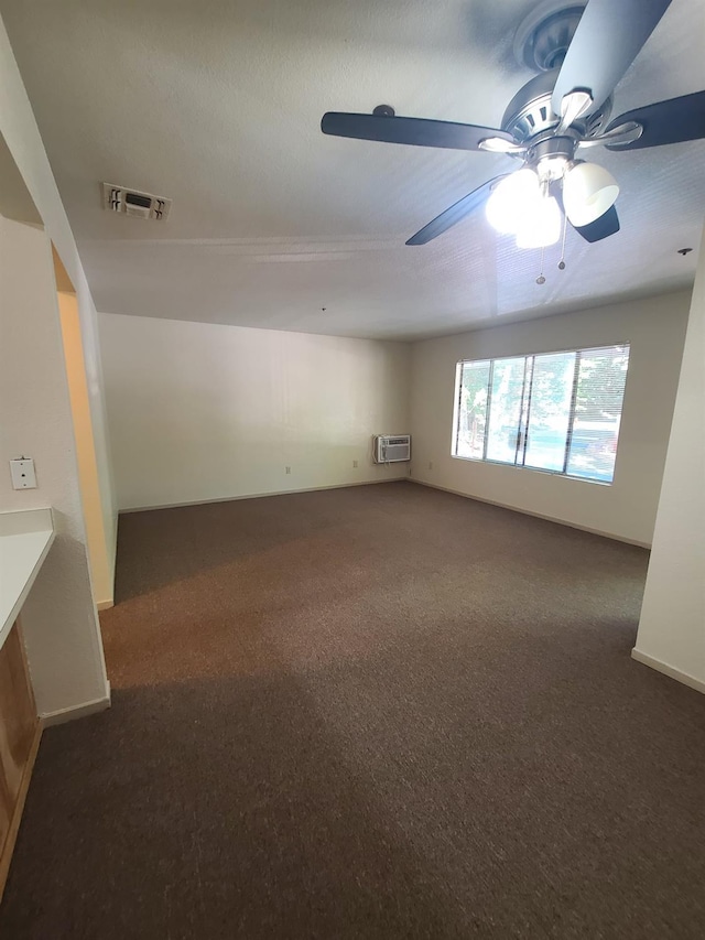 empty room with a wall unit AC, visible vents, dark carpet, a ceiling fan, and baseboards