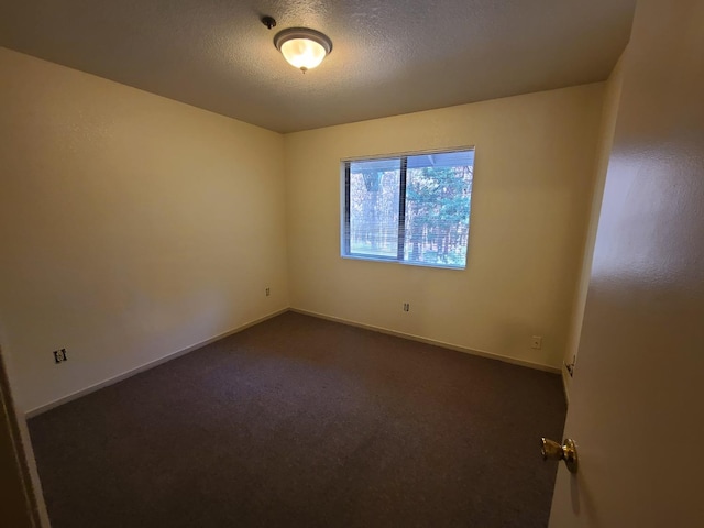 unfurnished room featuring a textured ceiling, dark colored carpet, and baseboards