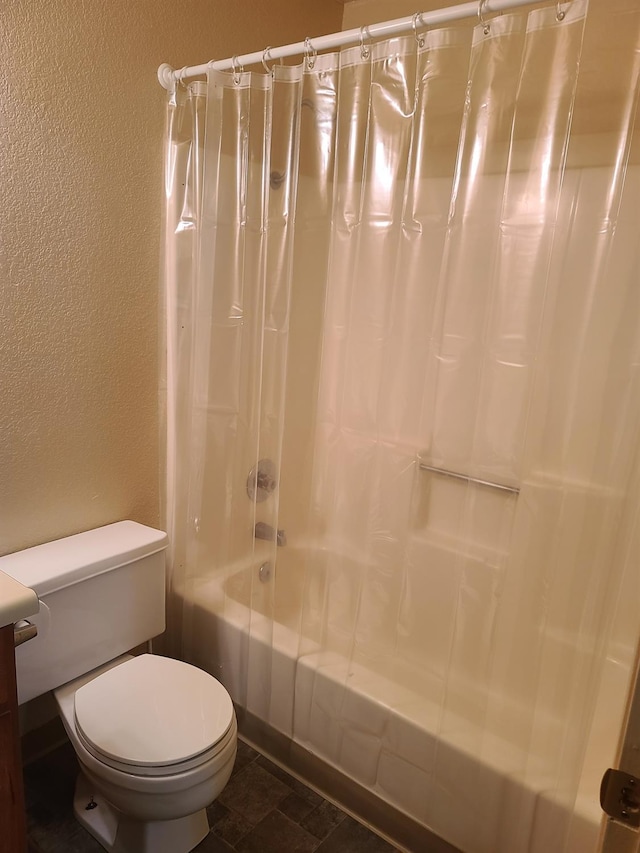 full bath featuring toilet, shower / bath combo with shower curtain, and a textured wall