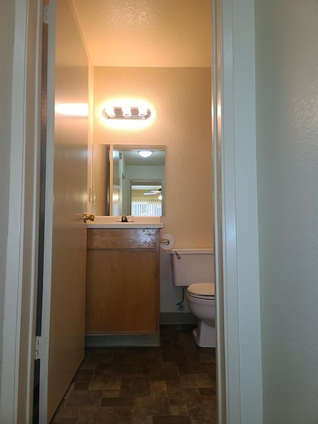 bathroom with a textured wall, stone finish flooring, vanity, and toilet